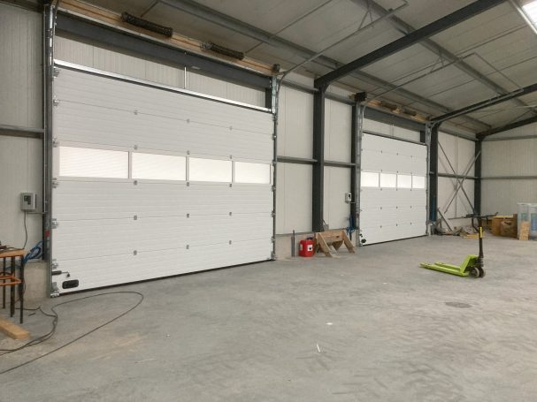 Intérieur d'un bâtiment avec deux grandes portes de garage fermées. Sol en béton.