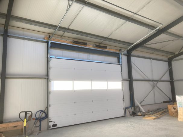 Porte sectionnelle blanche dans un entrepôt avec structures métalliques au fond.