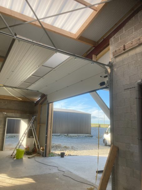 Porte de garage ouverte dans un bâtiment en construction, vue extérieure sur un paysage.