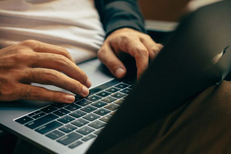 Homme tapant sur un ordinateur portable, mains sur le clavier, assis dans un canapé.