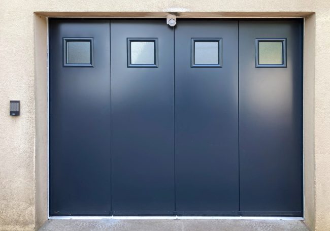 Porte de garage en métal gris avec trois fenêtres carrées en haut.