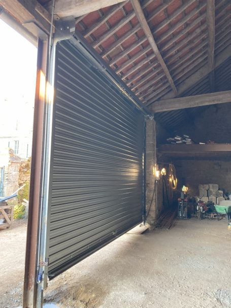 Porte roulante grise ouverte dans un garage en pierre.